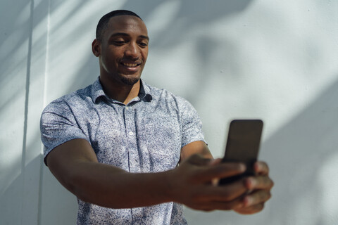 Lächelnder junger Mann mit Hemd, der ein Selfie an einer Wand macht, lizenzfreies Stockfoto