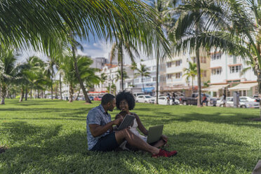 USA, Florida, Miami Beach, junges Paar mit Tablet und Laptop auf Rasen in einem Park - BOYF00861