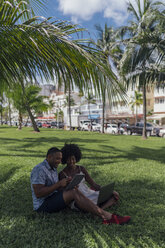USA, Florida, Miami Beach, junges Paar mit Tablet und Laptop auf Rasen in einem Park - BOYF00862