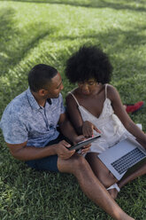 Junges Paar benutzt Tablet und Laptop auf einer Wiese in einem Park - BOYF00863