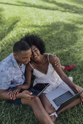 Glückliches junges Paar mit Tablet und Laptop auf einer Wiese in einem Park - BOYF00864