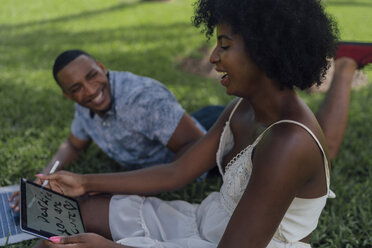 Glückliche junge Frau mit ihrem Freund in einem Park, der ein Tablet benutzt - BOYF00870