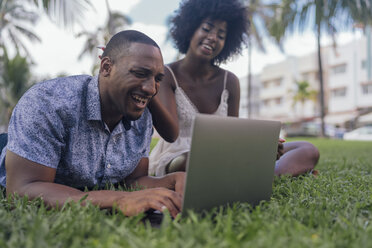 USA, Florida, Miami Beach, lachendes junges Paar mit Laptop auf dem Rasen in einem Park - BOYF00879