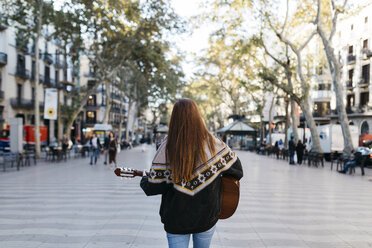 Red-haired woman playing the guitar in the city, rear view - JRFF01921