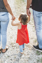 Mädchen geht auf einem Feldweg an den Händen der Eltern - HMEF00053