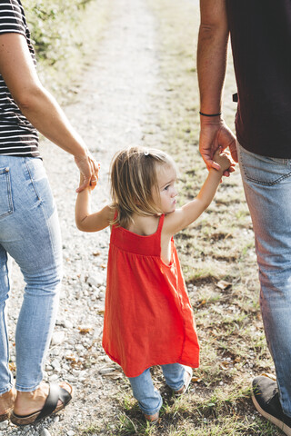 Girl walking on parent's hands on a field path stock photo