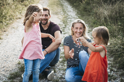 Glückliche Familie mit zwei Töchtern spielt mit Konfetti auf einem Feldweg, lizenzfreies Stockfoto