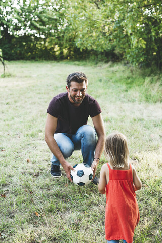 Glücklicher Vater spielt mit seiner Tochter auf einer Wiese Fußball, lizenzfreies Stockfoto