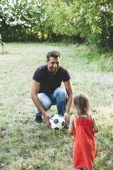 Glücklicher Vater spielt mit seiner Tochter auf einer Wiese Fußball - HMEF00058