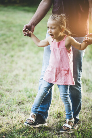 Mädchen läuft auf der Wiese auf den Füßen des Vaters, lizenzfreies Stockfoto