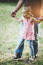 Girl walking on father's feet on meadow - HMEF00065