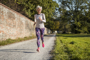 Senior woman running along brick wall in a park - DIGF05435