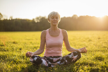 Senior woman in lotus position on rural meadow at sunset - DIGF05467