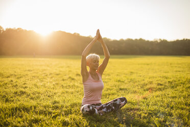 Ältere Frau macht Yoga auf einer ländlichen Wiese bei Sonnenuntergang - DIGF05471