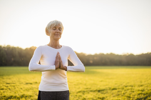 Ältere Frau macht Yoga auf einer ländlichen Wiese bei Sonnenuntergang, lizenzfreies Stockfoto