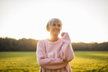 Portrait of smiling senior woman standing on rural meadow at sunset - DIGF05484