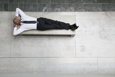 A view looking down on a businessman taking a break laying down on a bench. - MINF09536