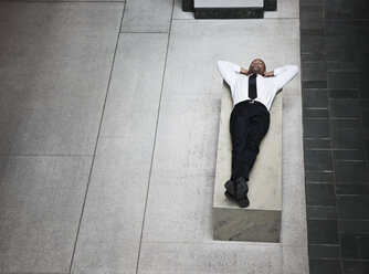 A view looking down on a businessman taking a break laying down on a bench. - MINF09537