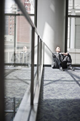 Low view looking at a Caucasian businessman taking a break sitting at the base of a column in a convention centre space. - MINF09548