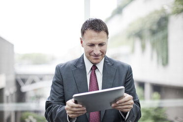 A Caucasian businessman checking his notebook computer while standing in a convention cener lobby. - MINF09554