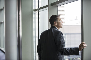 A Caucasian businessman standing next to and looking out of a large window in a convention centre. - MINF09556