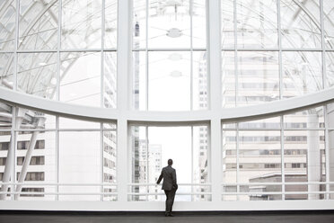 A businessman in silhouette standing at a large window in a convention centre lobby. - MINF09558