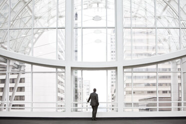 Ein Geschäftsmann in Silhouette steht an einem großen Fenster in der Lobby eines Kongresszentrums. - MINF09558