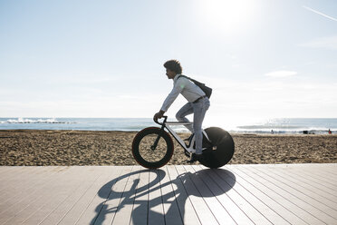 Mittlerer erwachsener Mann fährt Fahrrad auf einer Strandpromenade, hört Musik - JRFF01942