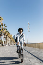 Mittlerer erwachsener Mann fährt Fahrrad auf einer Strandpromenade, hört Musik - JRFF01943