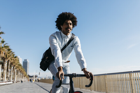 Mittlerer erwachsener Mann fährt Fahrrad auf einer Strandpromenade, hört Musik, lizenzfreies Stockfoto