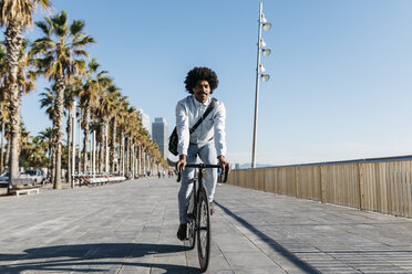 Mittlerer erwachsener Mann fährt Fahrrad auf einer Strandpromenade, hört Musik - JRFF01945