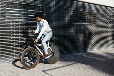 Mittelgroßer erwachsener Mann fährt mit dem Fahrrad und benutzt ein Smartphone - JRFF01946