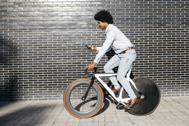 Mittelgroßer erwachsener Mann fährt mit dem Fahrrad und benutzt ein Smartphone - JRFF01947
