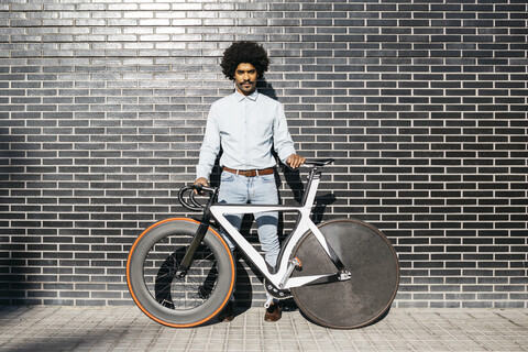 Mittlerer erwachsener Mann vor schwarzer Wand stehend, sein Fahrrad haltend, lizenzfreies Stockfoto