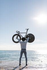 Mann, der sein Fahrrad am Strand anhebt und das Meer beobachtet - JRFF01963