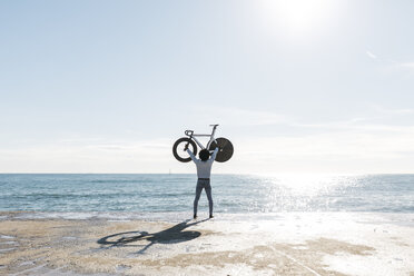 Man lifting his bike on the beach, watching the sea - JRFF01964