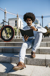 Mittlerer erwachsener Mann mit Fahrrad auf einer Treppe sitzend, in einem Buch lesend - JRFF01967