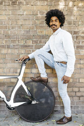 Stolzer Mann steht mit seinem Fixie-Fahrrad vor einer Backsteinmauer - JRFF01972