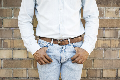 Mittlerer erwachsener Mann vor einer Backsteinmauer stehend, mittlerer Schnitt, Hände in den Taschen, lizenzfreies Stockfoto