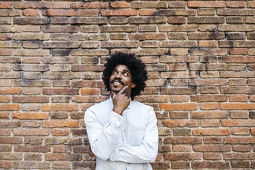 Mid adult man standing in front of brick wall, looking up, smiling - JRFF01977