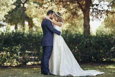 Bridal couple standing head to head with eyes closed in a park - JSMF00567