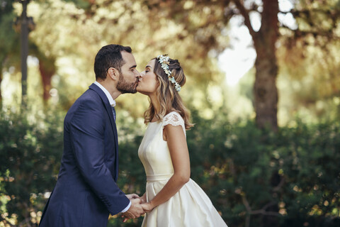 Brautpaar, das sich im Park küsst und die Hände hält, lizenzfreies Stockfoto