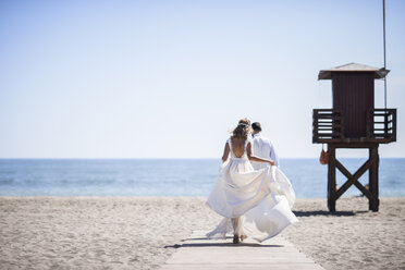 Back view of bridal couple enjoying wedding day walking on the beach - JSMF00584