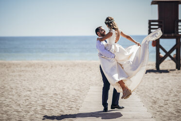 Ein glückliches Brautpaar, das seinen Hochzeitstag am Strand genießt - JSMF00586