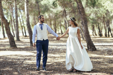 Happy bridal couple walking hand in hand in pine forest - JSMF00590