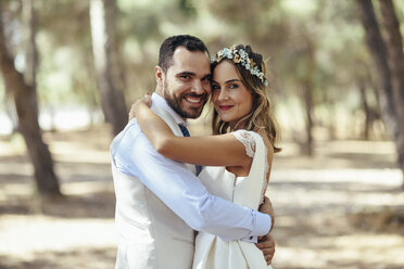 Portrait of happy bridal couple standing head to head in pine forest - JSMF00593