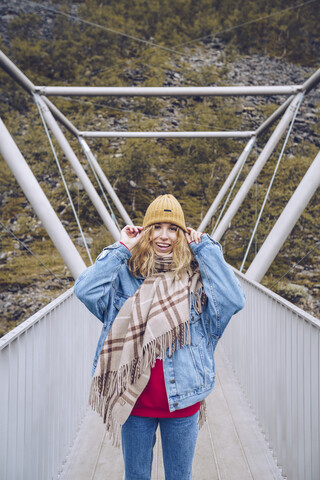 Young woman standing on a windy bridge, holding her cap stock photo