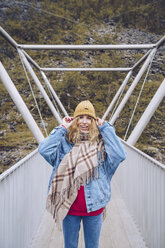 Junge Frau steht auf einer windigen Brücke und hält ihre Mütze - RSGF00089