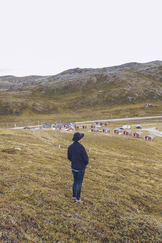 Junger Mann auf einem Hügel stehend, Blick auf eine Siedlung, Nordkap, Norwegen, lizenzfreies Stockfoto