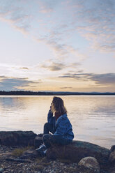 Young woman sitting at lake Inari, looking at view, Finland - RSGF00094